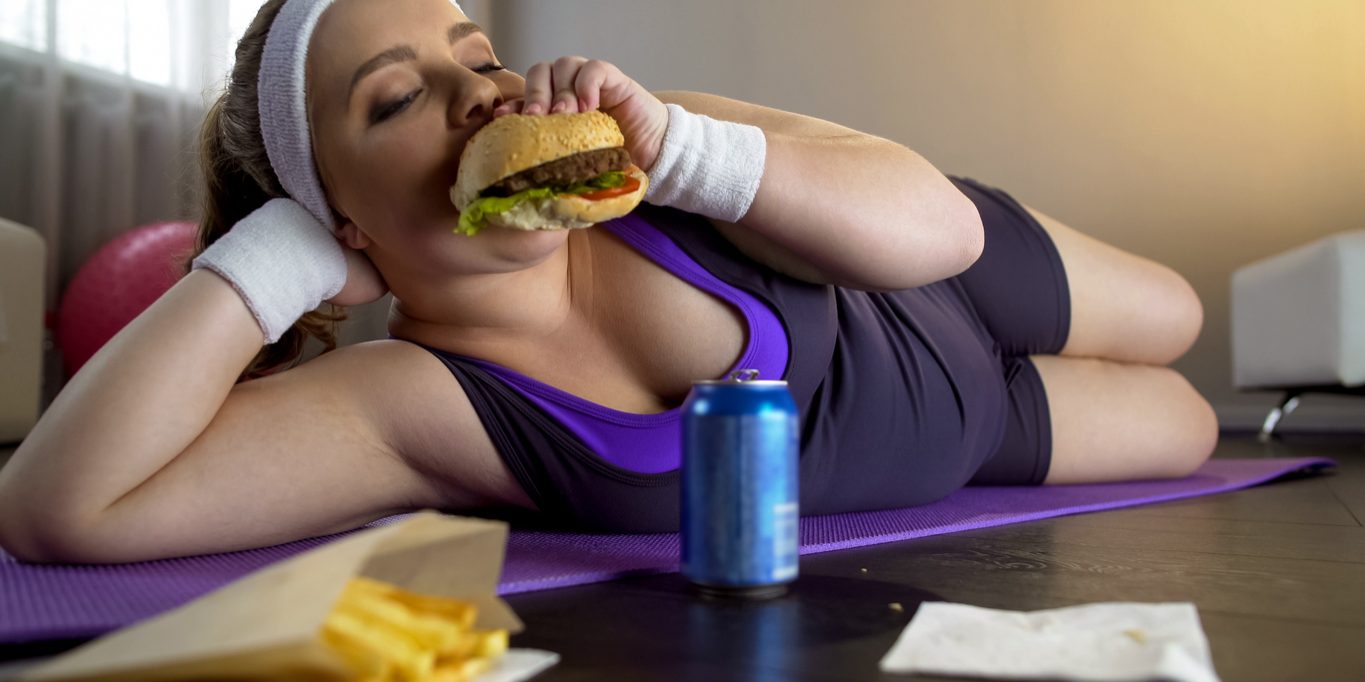 Obese female eating greasy burger instead of sports workout, lack of motivation