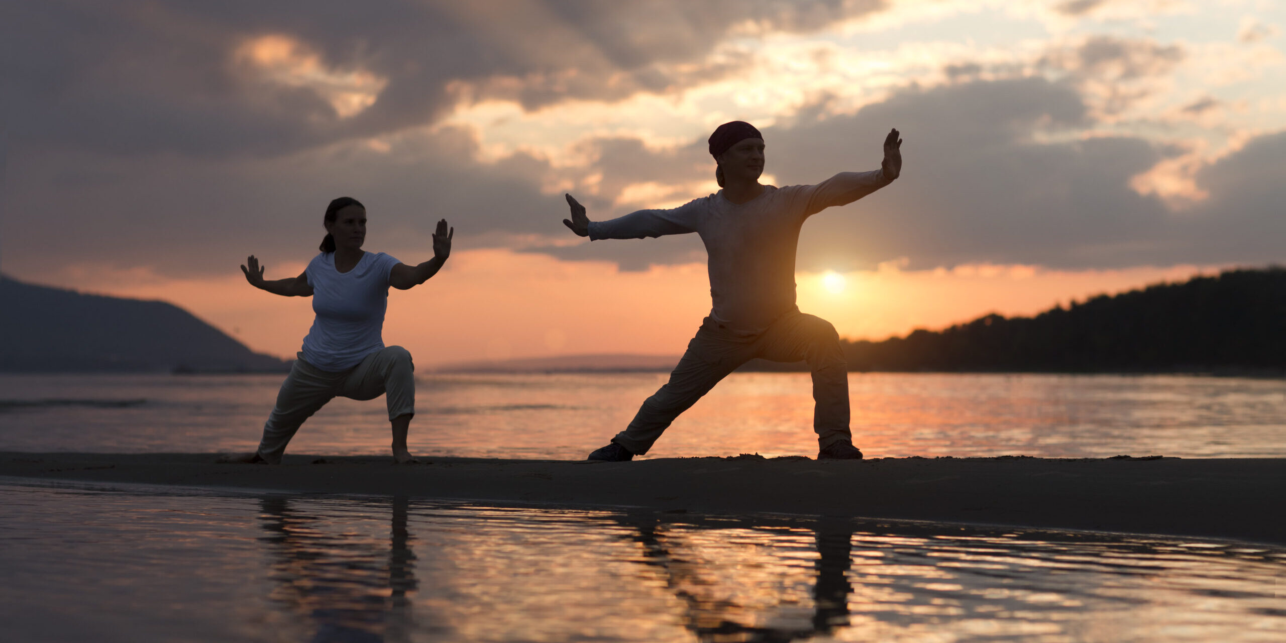 Man and woman doing Tai Chi chuan at sunset on the beach.  solo outdoor activities. Social Distancing. Healthy lifestyle  concept.