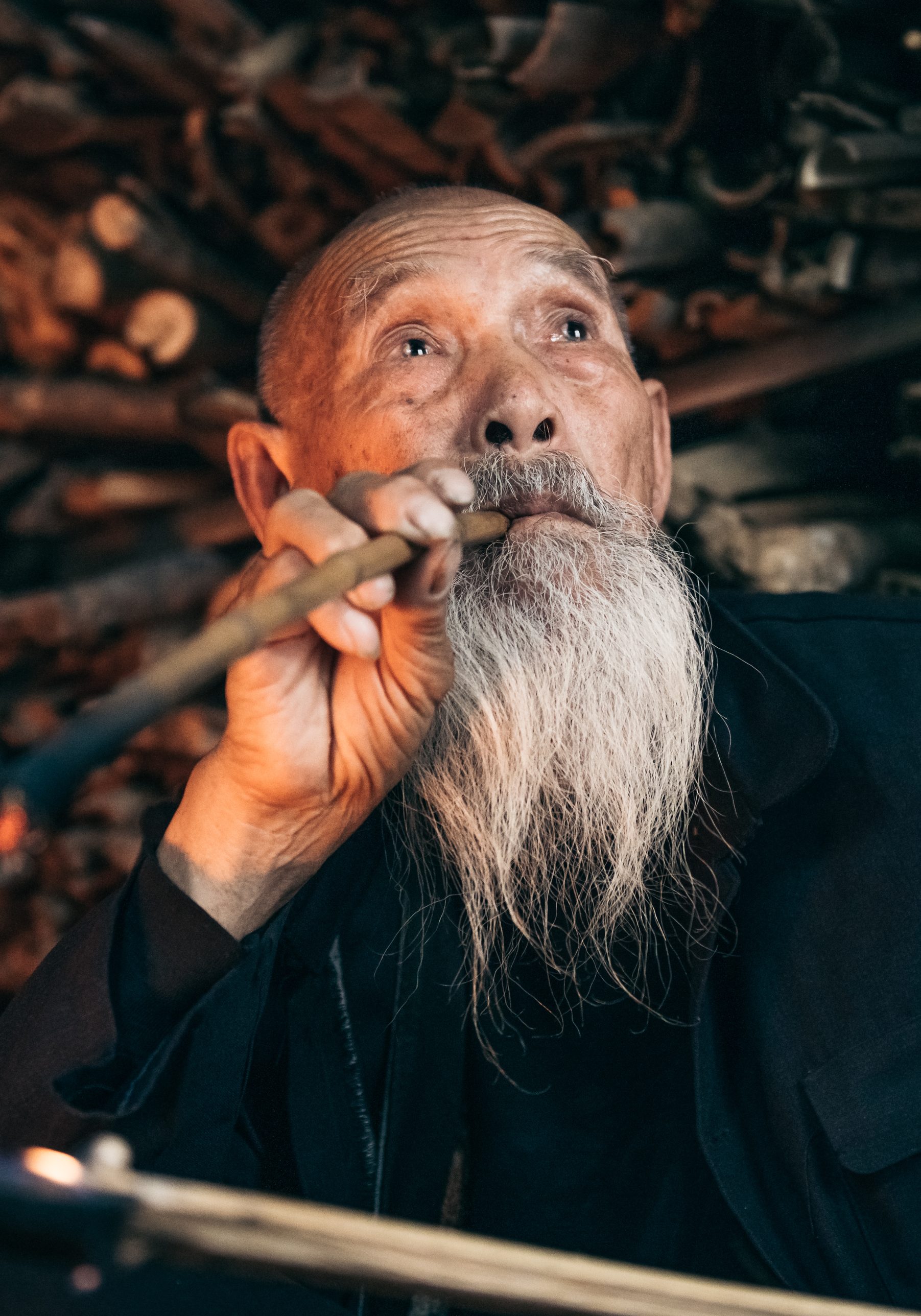 old pensive chinese senior man smoking pipe in simple wooden hut